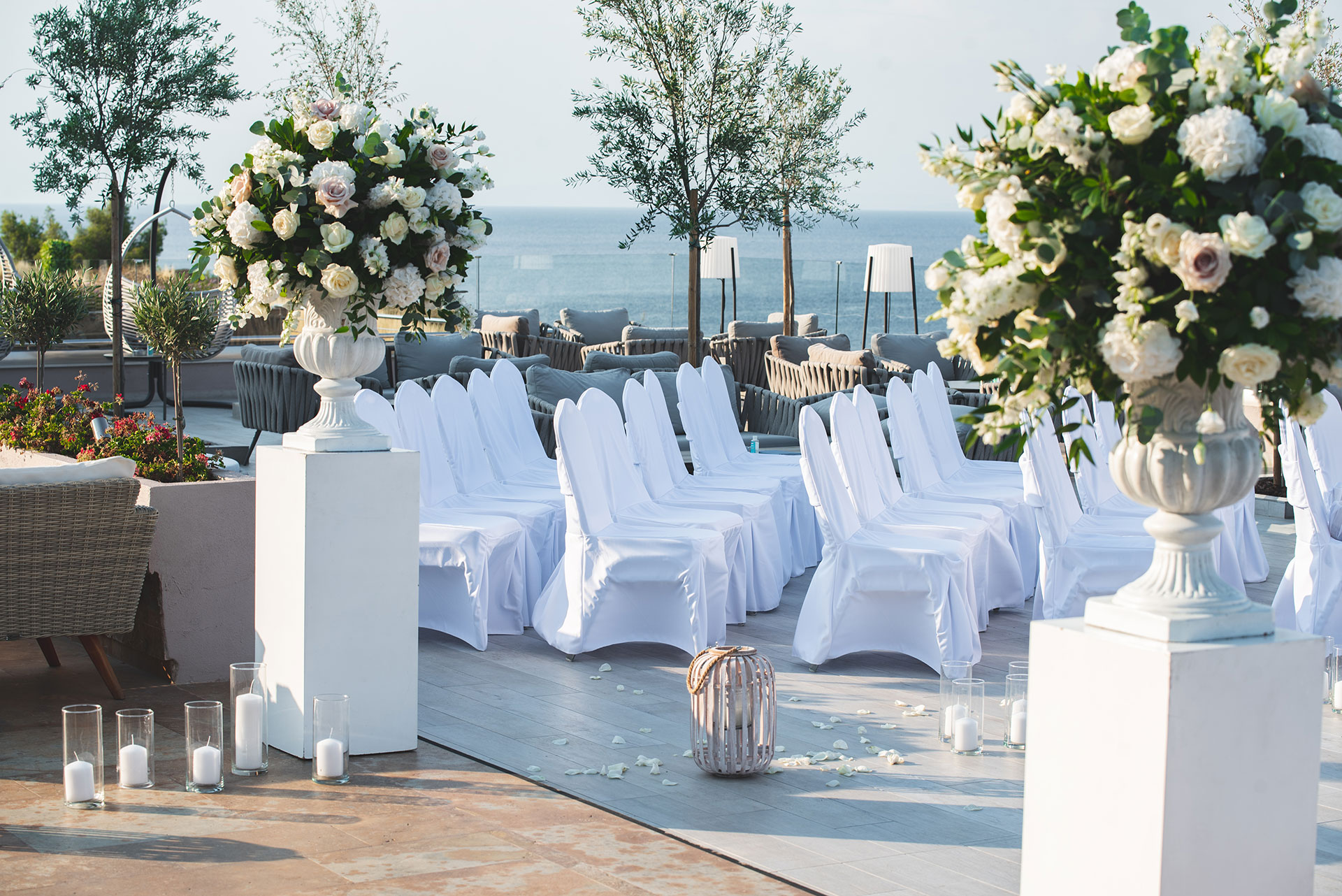 Elegant seaside wedding setup with white chairs, floral arrangements and sea view