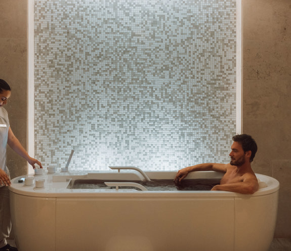 Spa therapist assisting a man relaxing in a jacuzzi with tiled wall backdrop 