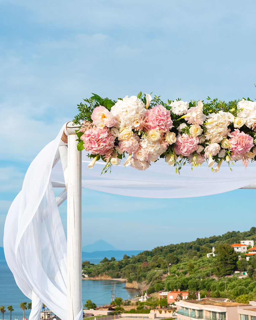 Floral wedding arch with pink and white roses overlooking the sea and hills