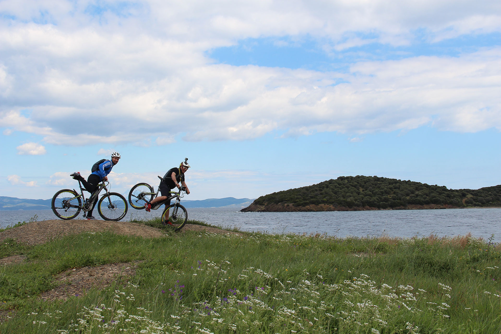 Two cyclists riding along the seaside road surrounded by greenery