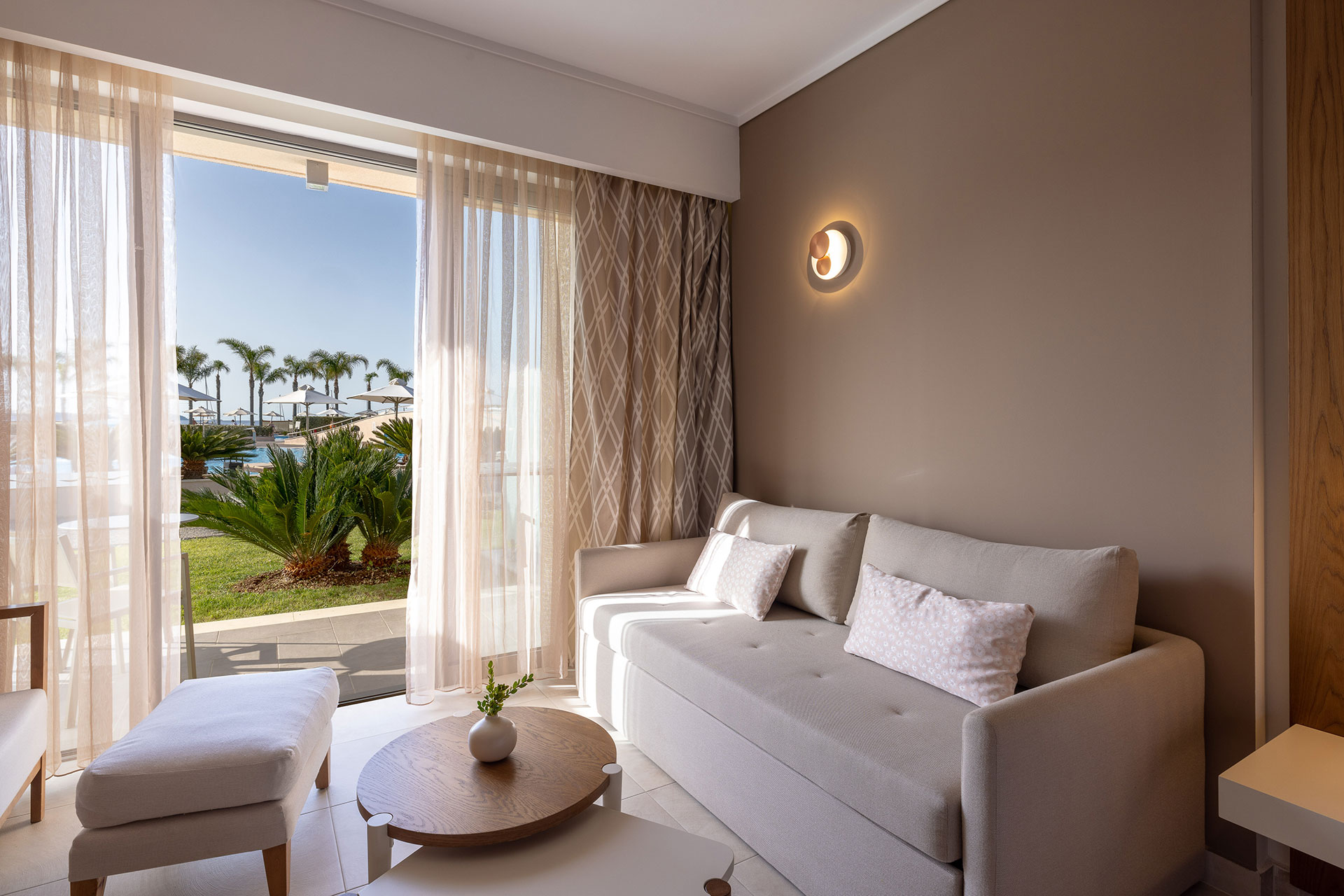 Seating area of deluxe room with soft cozy sofa, modern decor and pool view