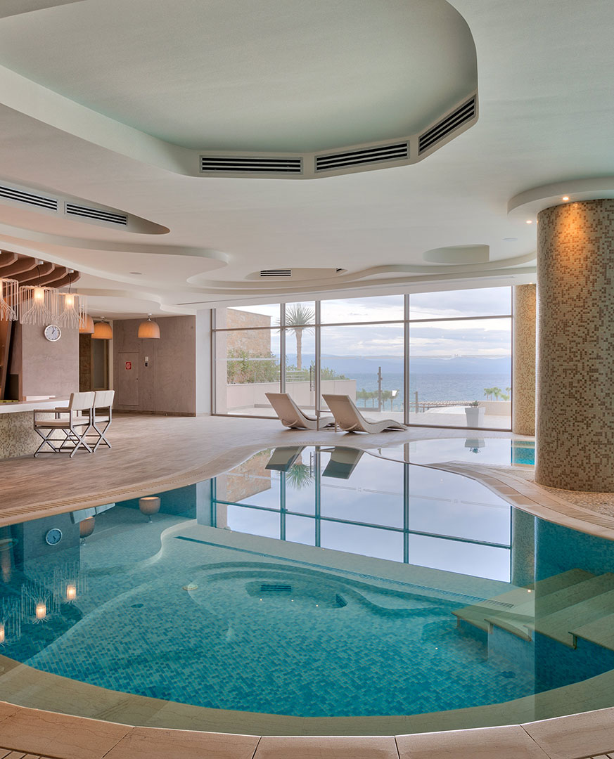 Modern indoor thermal pool with sea view and relaxing loungers