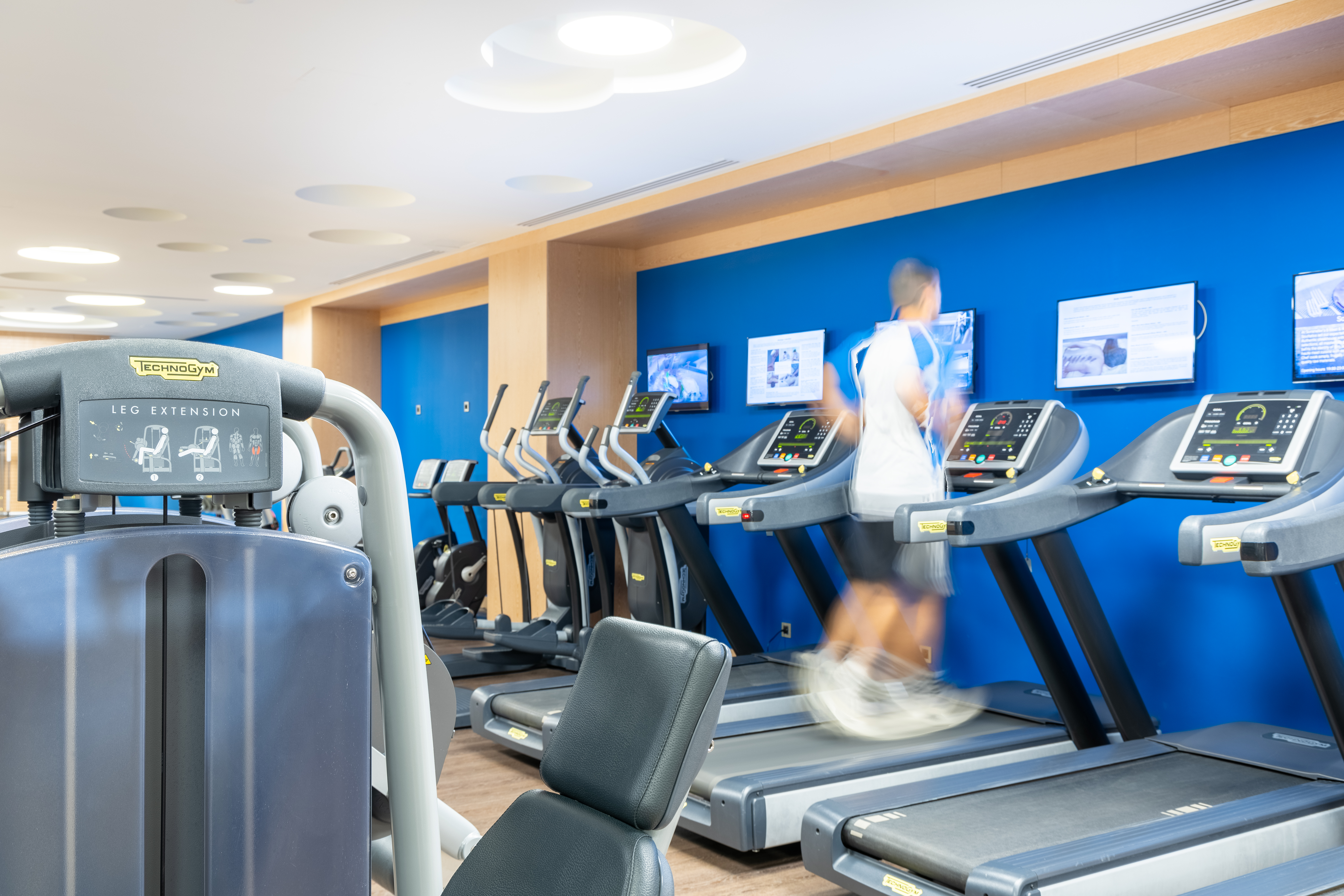 Man running on treadmill inside the bright modern gym with training equipment