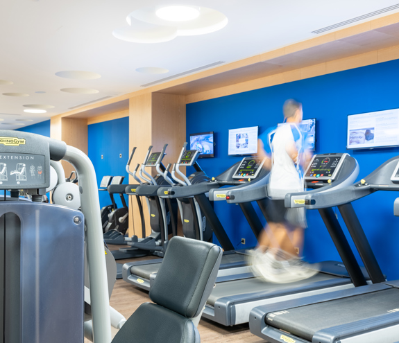 Man running on treadmill inside the bright modern gym with training equipment