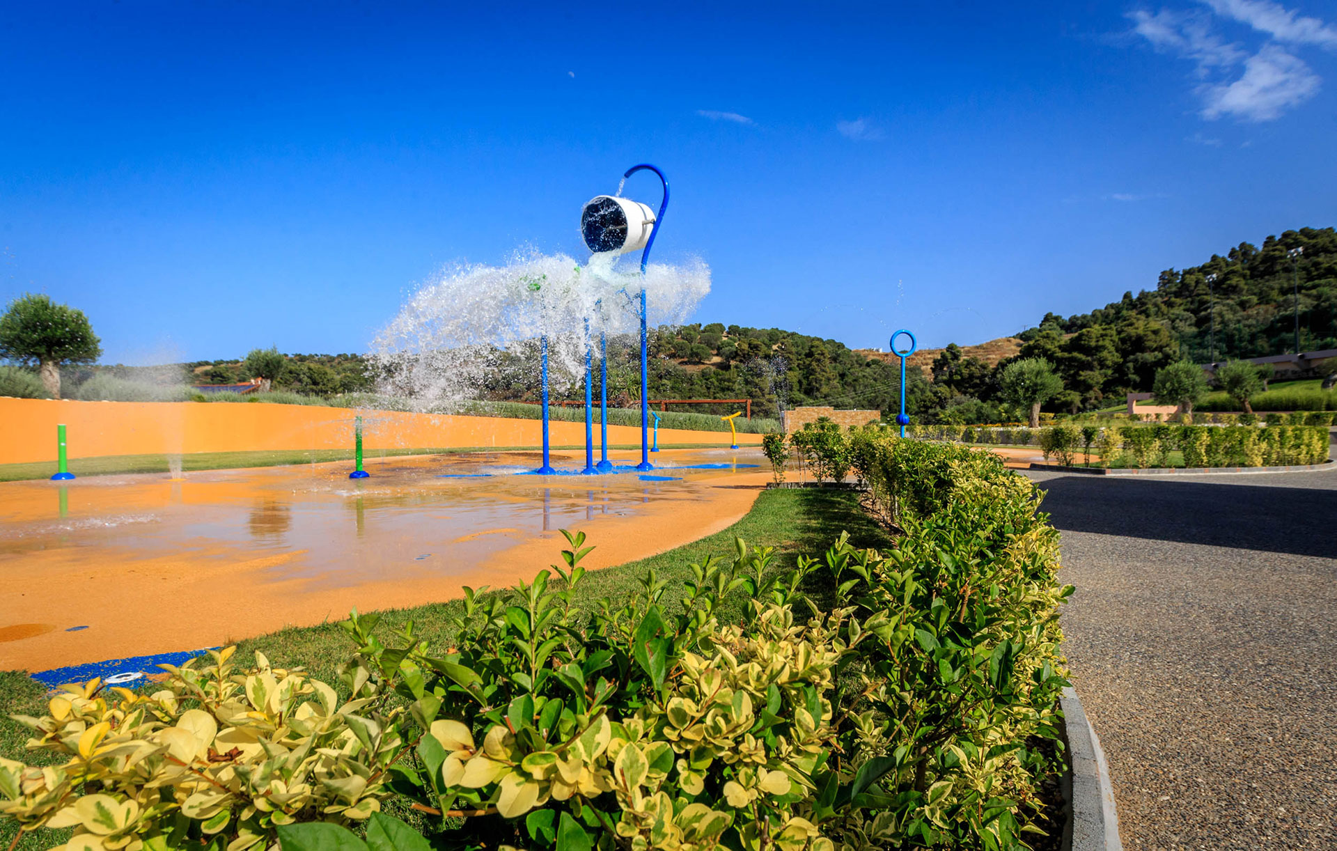 Outdoor splash park with tipping buckets and water jets under a bright blue sky