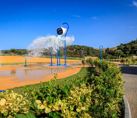 Outdoor splash park with tipping buckets and water jets under a bright blue sky