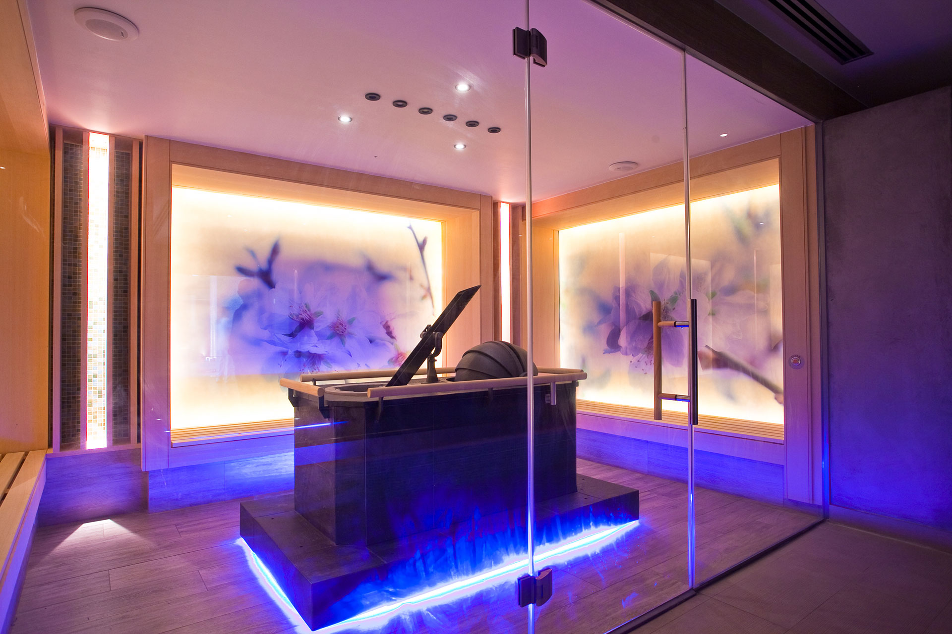 Modern sauna room with glass walls and ambient purple lighting 