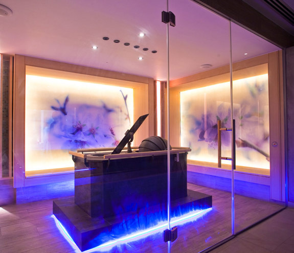 Modern sauna room with glass walls and ambient purple lighting 