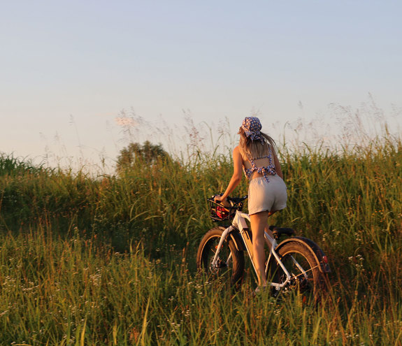 Woman cycling through tall grass at sunset on an electric bike