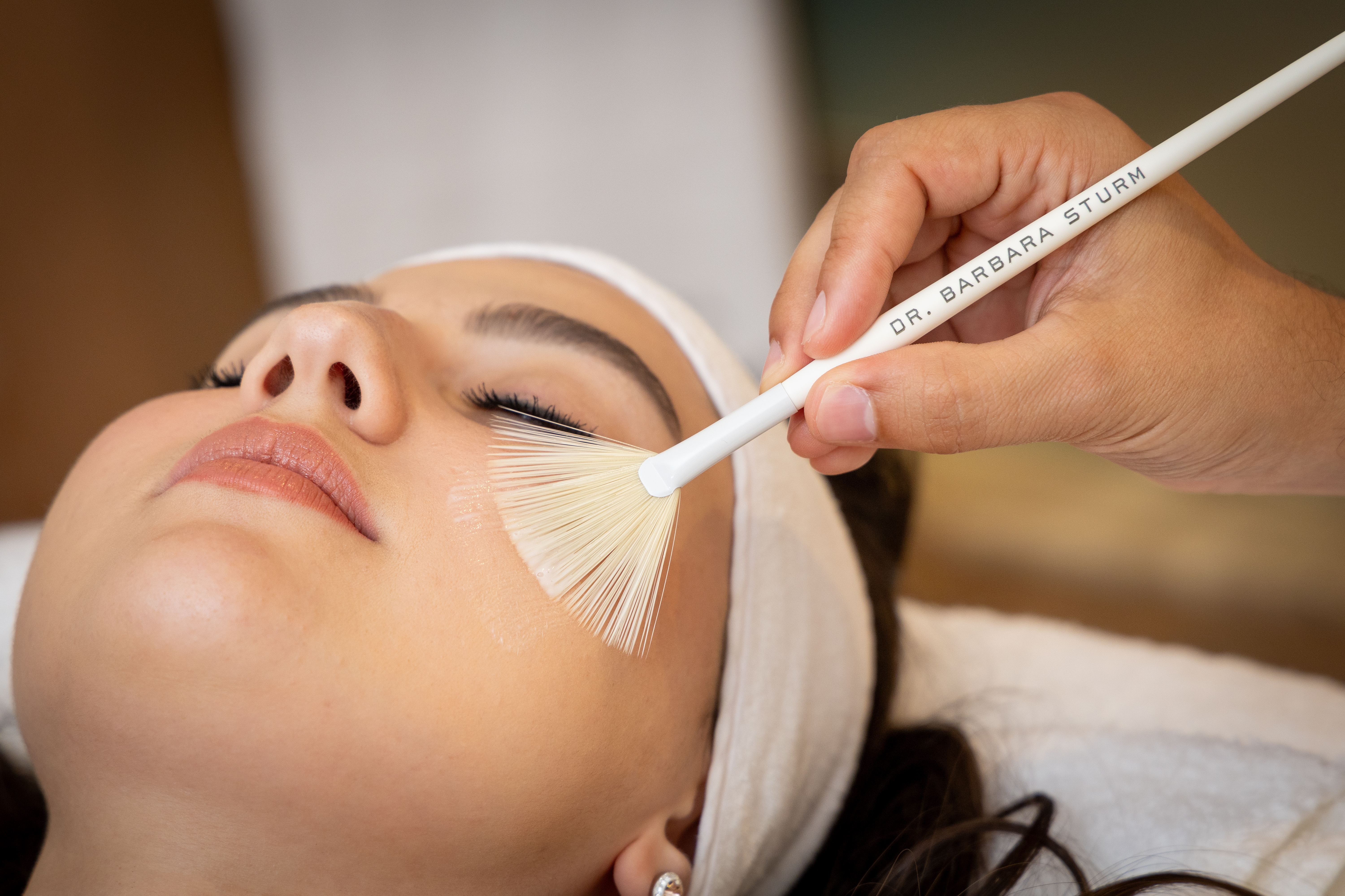 Therapist applying high end facial product with a brush to a woman's face in the treatment room