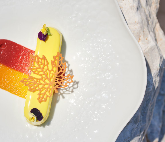 Elegant gourmet dessert with vibrant fruit purees and decorative sugar leaf garnish