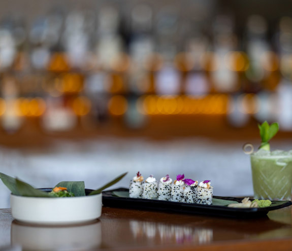Elegant sushi platter with green cocktail and bar backdrop