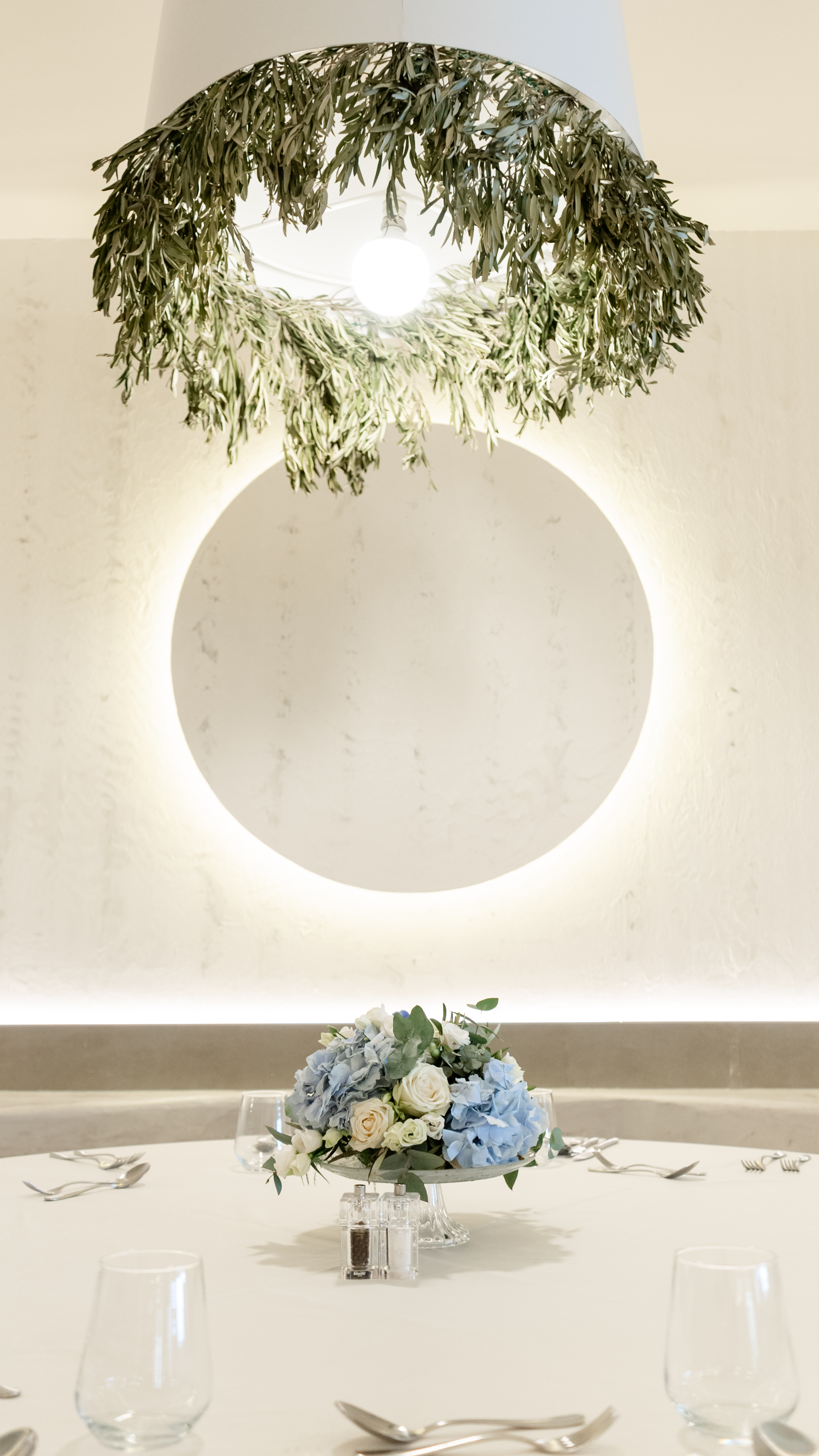 Decorative lighting with olive branches and floral arrangement on table under glowing circle