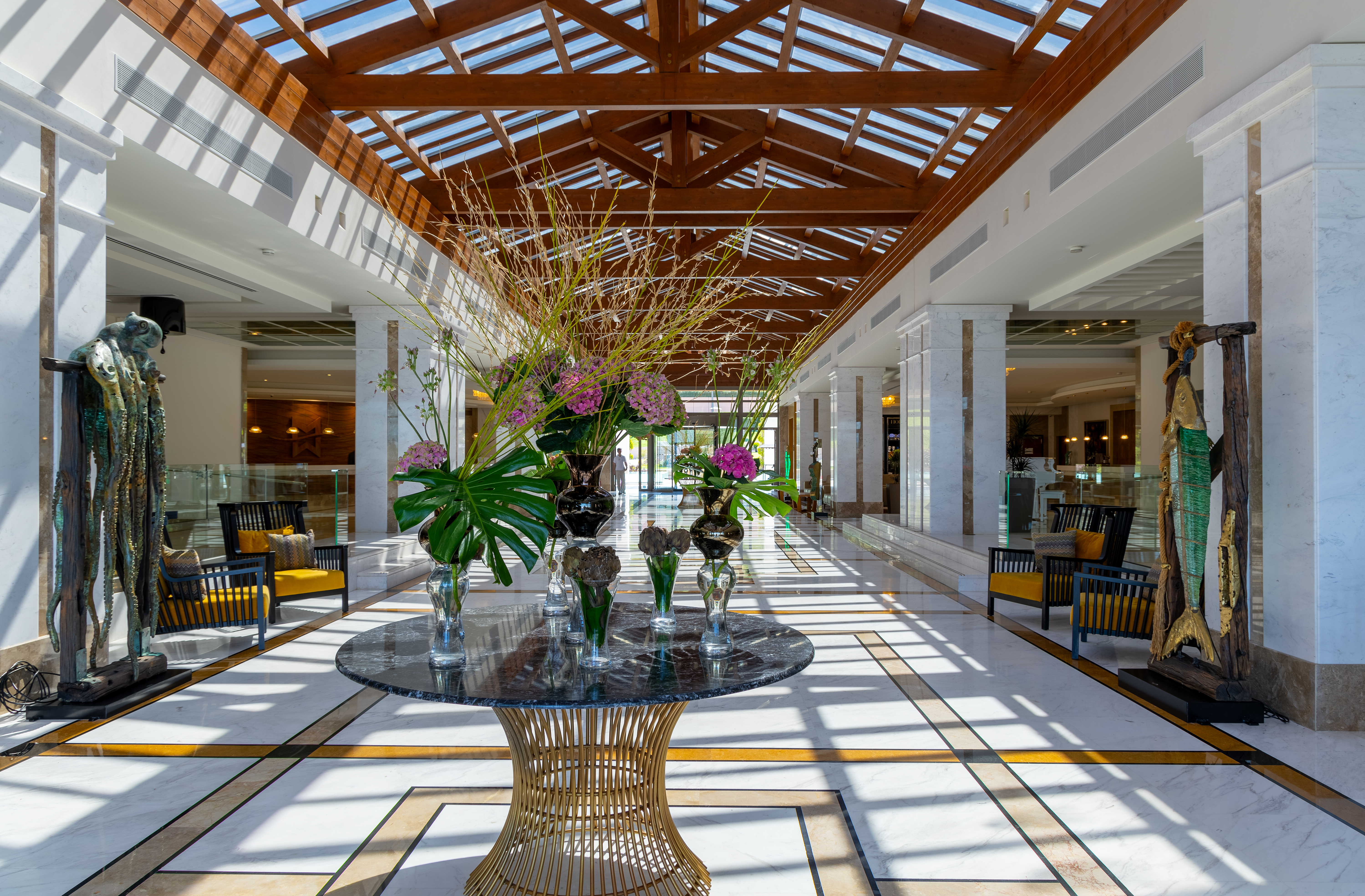 Elegant hotel lobby with glass roof, marble floors, and floral centerpiece