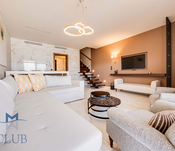Duplex suite's spacious living area, with warm lighting, wall mounted TV, and floating staircase