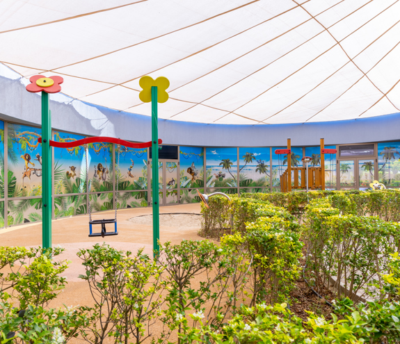 Shaded outdoor play area with swing and colorful wall murals at Kids Planet