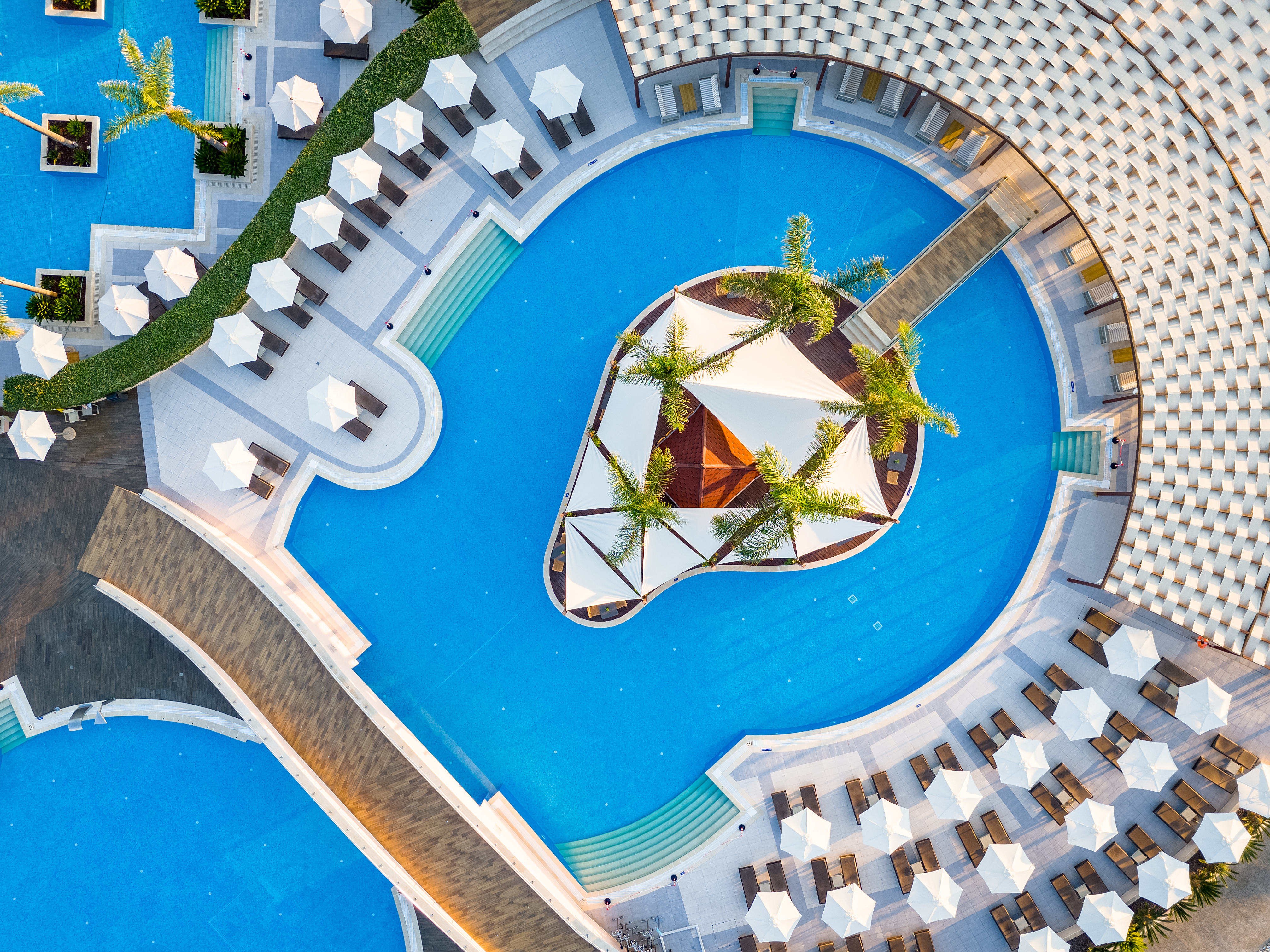 Top down view of the elegant central pool with white canopies, palm trees, and sun loungers