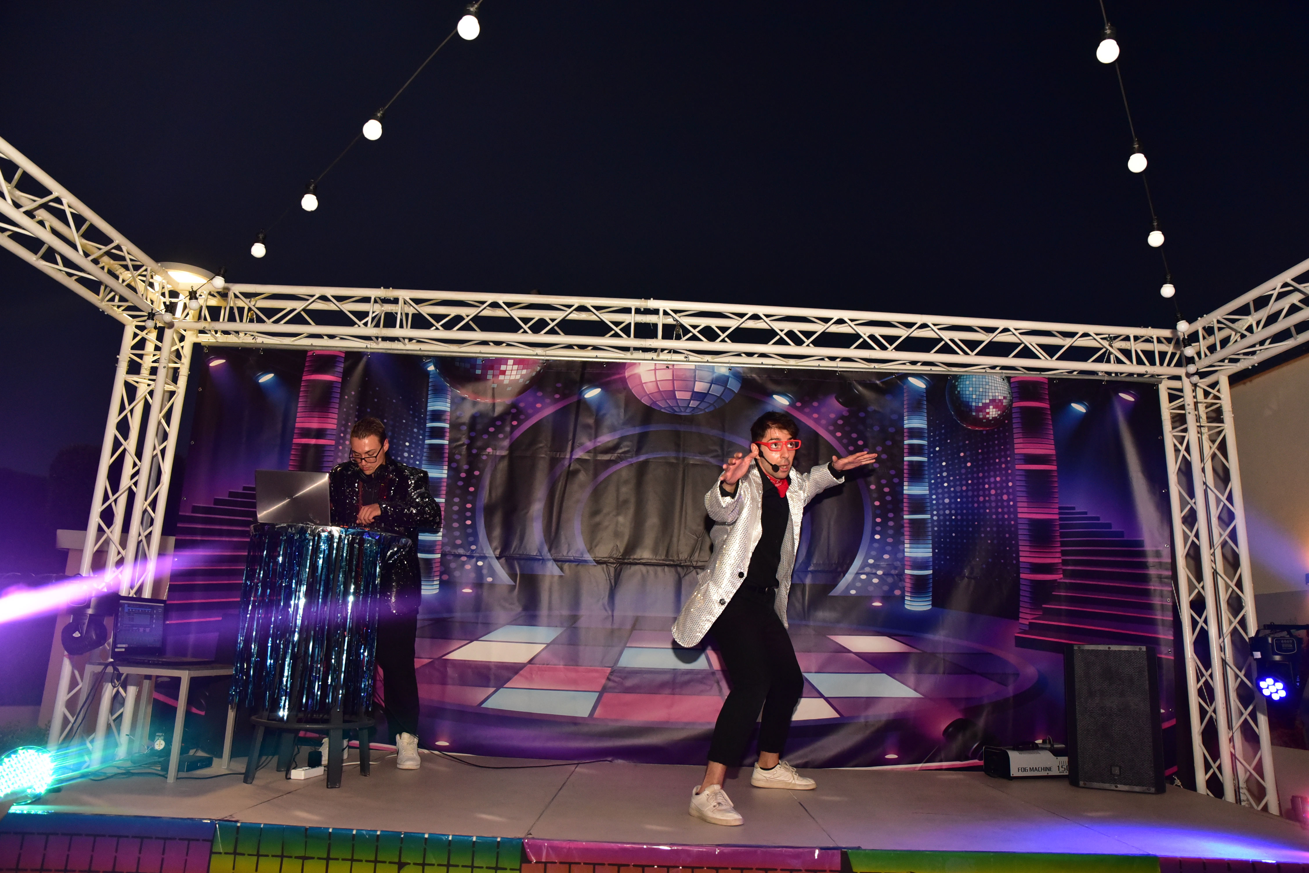 DJ and performer in sparkling disco outfits on illuminated stage during evening show