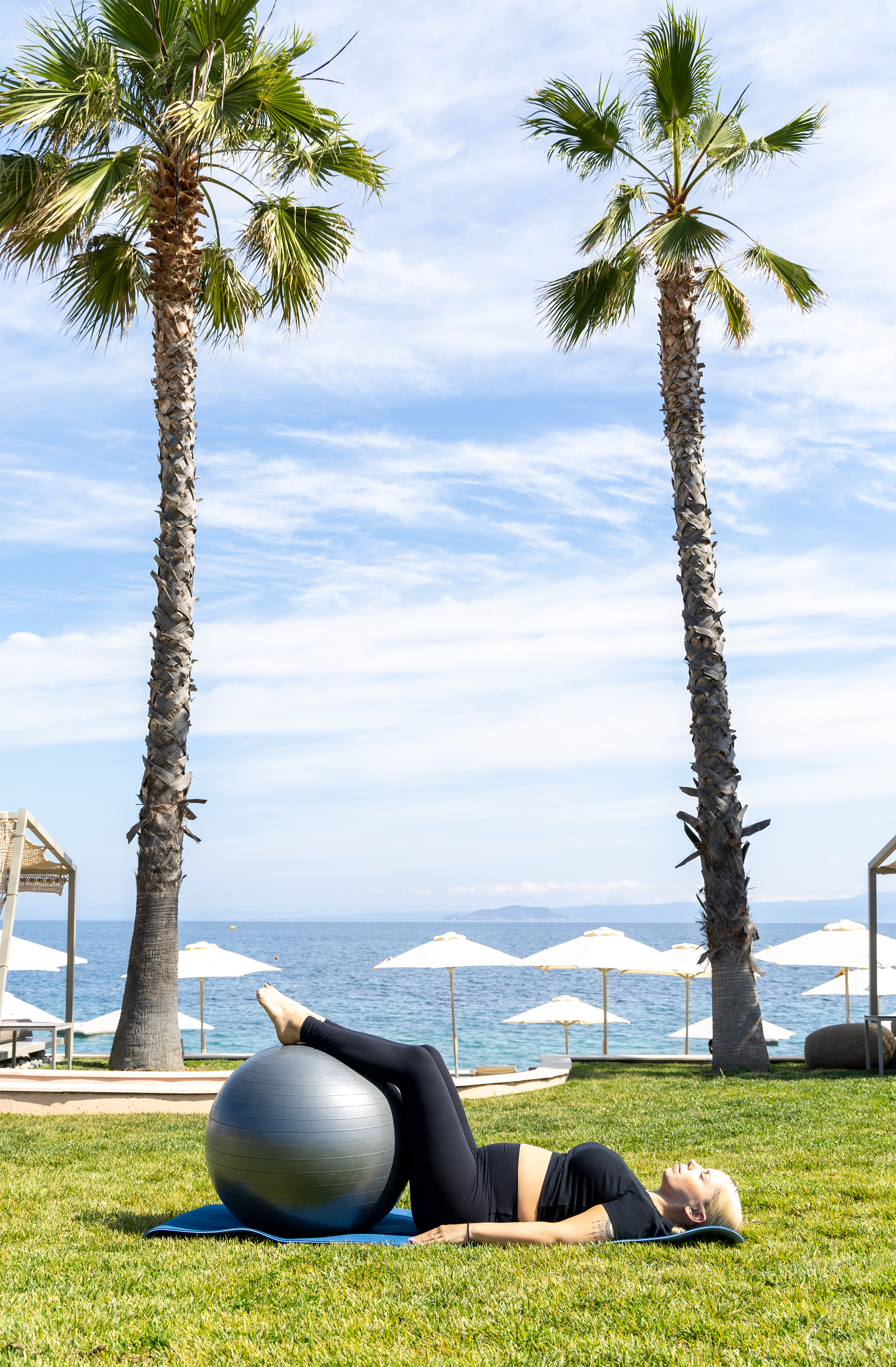 Outdoor fitness session with exercise ball under palm trees by the sea