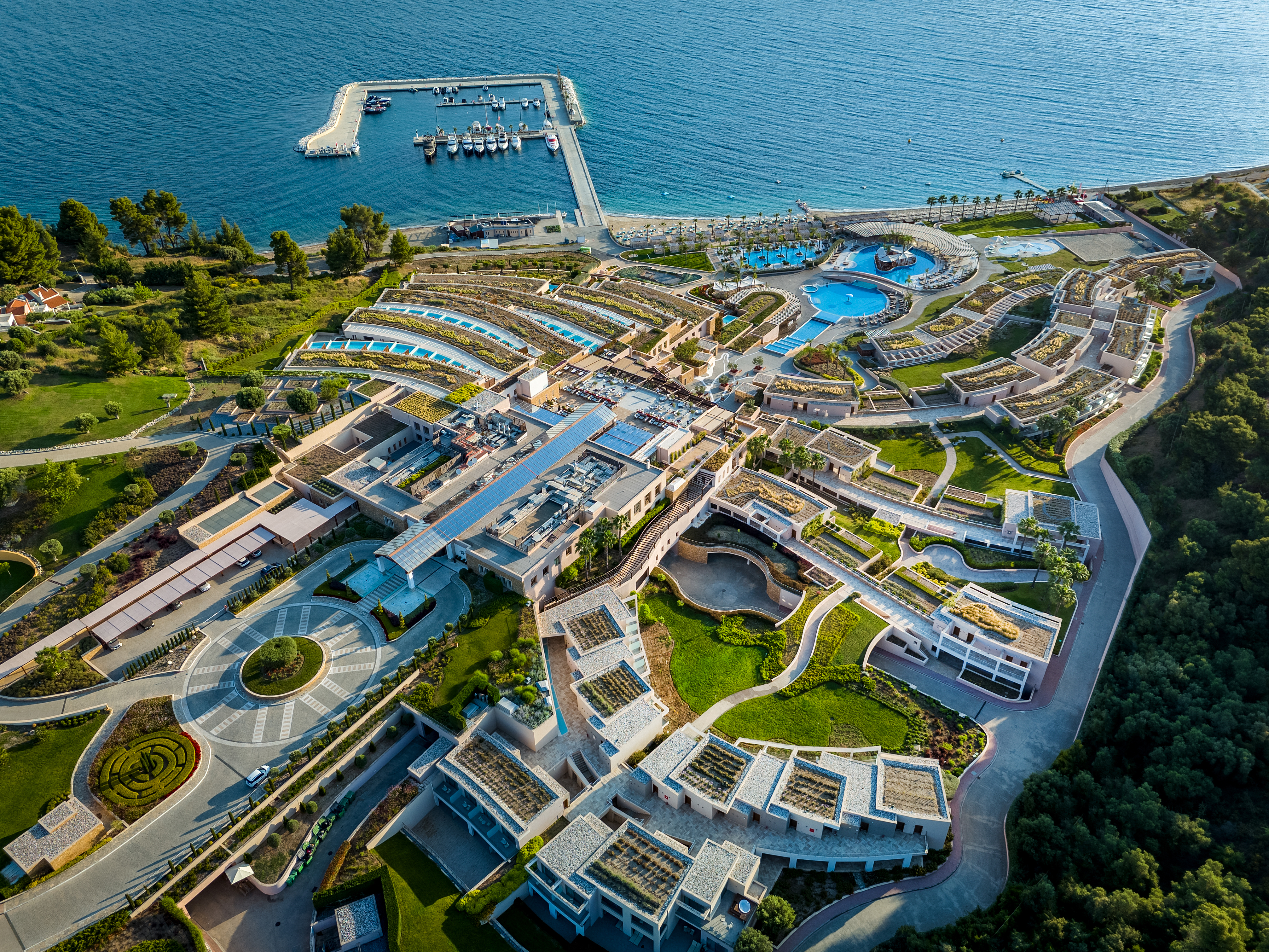 Aerial view of Miraggio Resort featuring its private marina, cascading architecture, and beachfront pools by the Aegean Sea