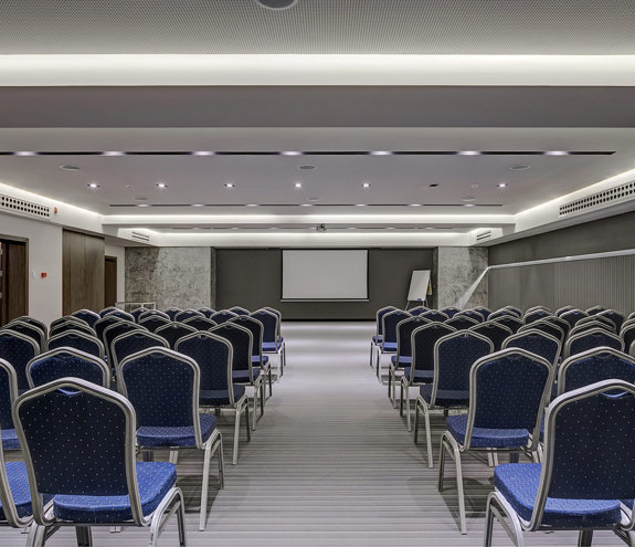 Modern conference room with rows of blue chairs, projector screen, and minimalist lighting
