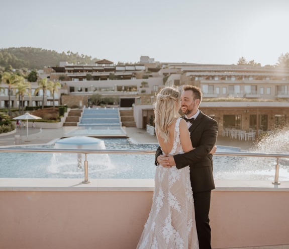 Bride and groom embracing by the pool with cascading water and resort view at sunset