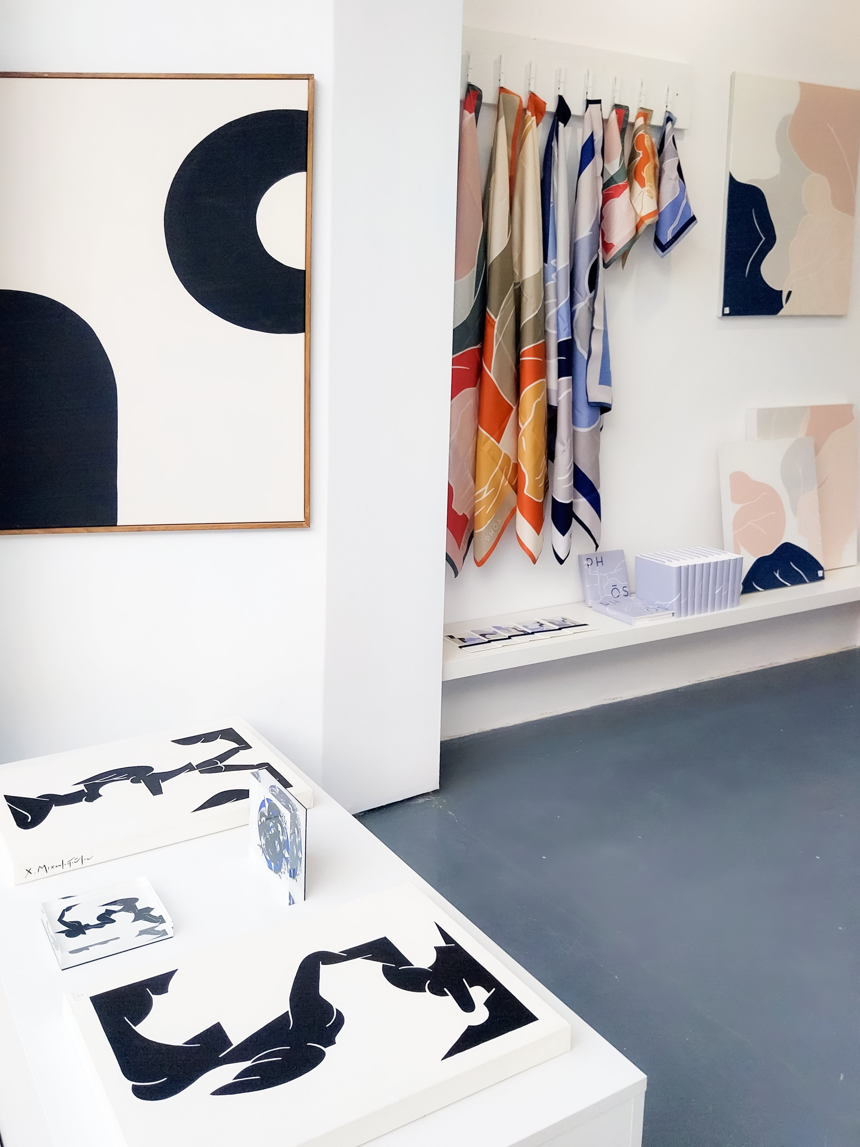 Large abstract paintings in deep blue tones displayed beside paster scarves