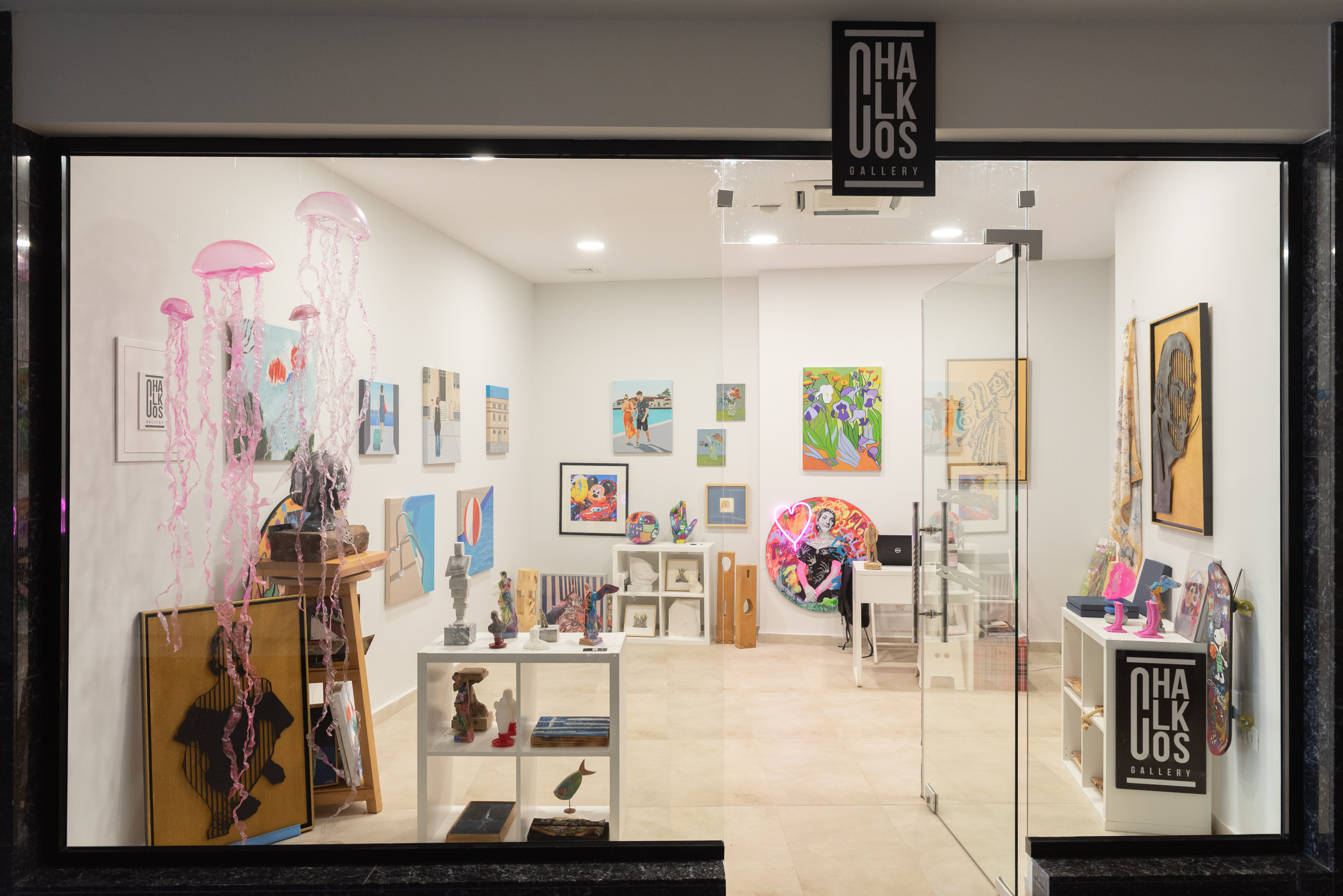 Chalkos Art Gallery storefront displaying sculptures, framed artworks, and pink jellyfish decorations hanging