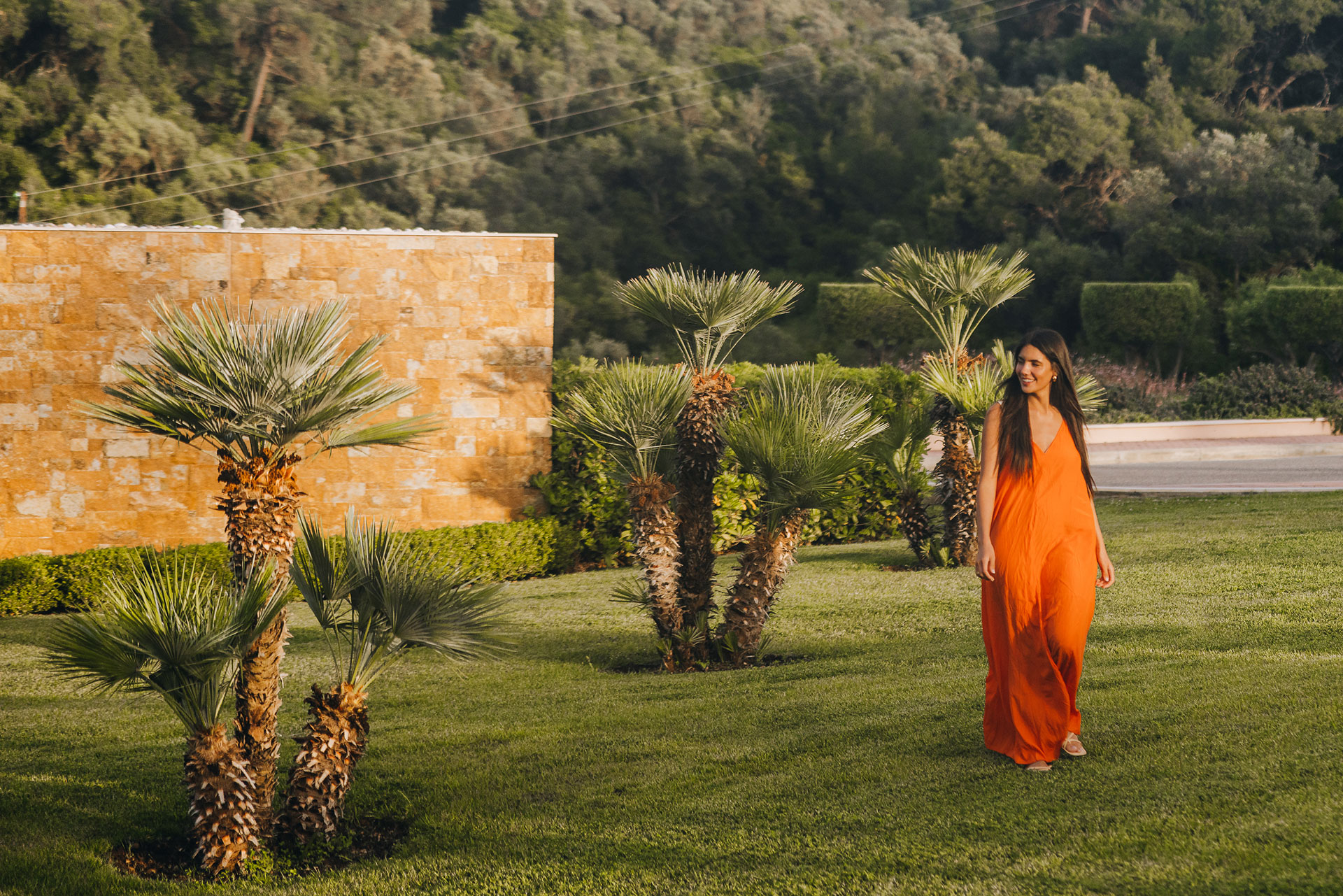 Woman in an orange dress walking through palm gardens at golden hour