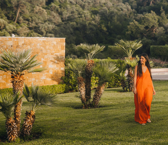 Woman in an orange dress walking through palm gardens at golden hour
