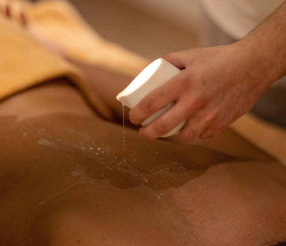 Therapist pouring warm essential oil on guest's back before massage