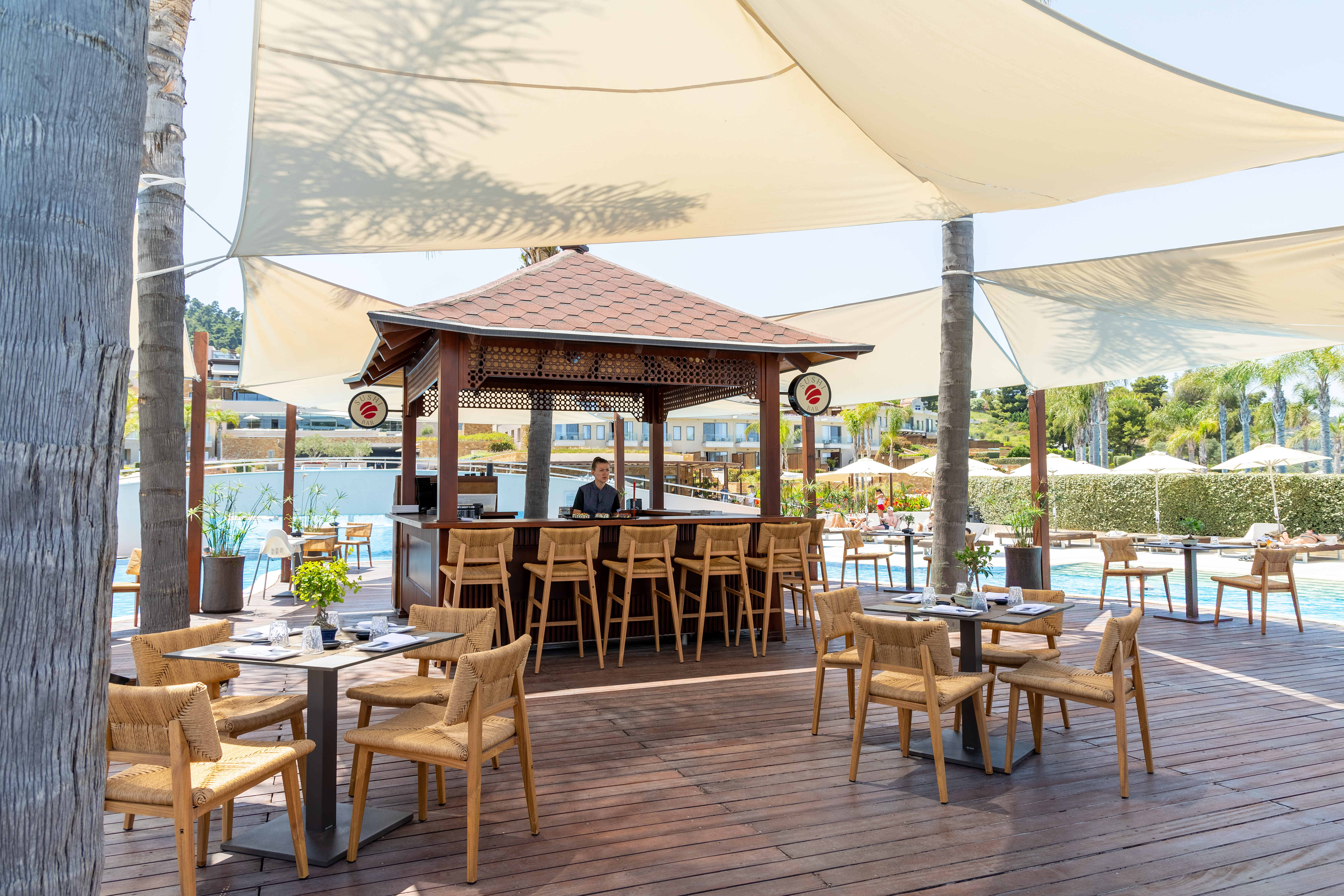 Outdoor sushi bar with wooden deck seating and shaded canopy by the pool