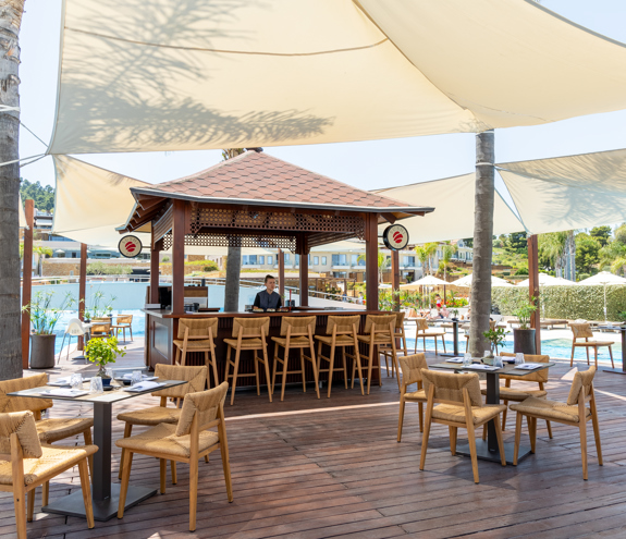 Outdoor sushi bar with wooden deck seating and shaded canopy by the pool