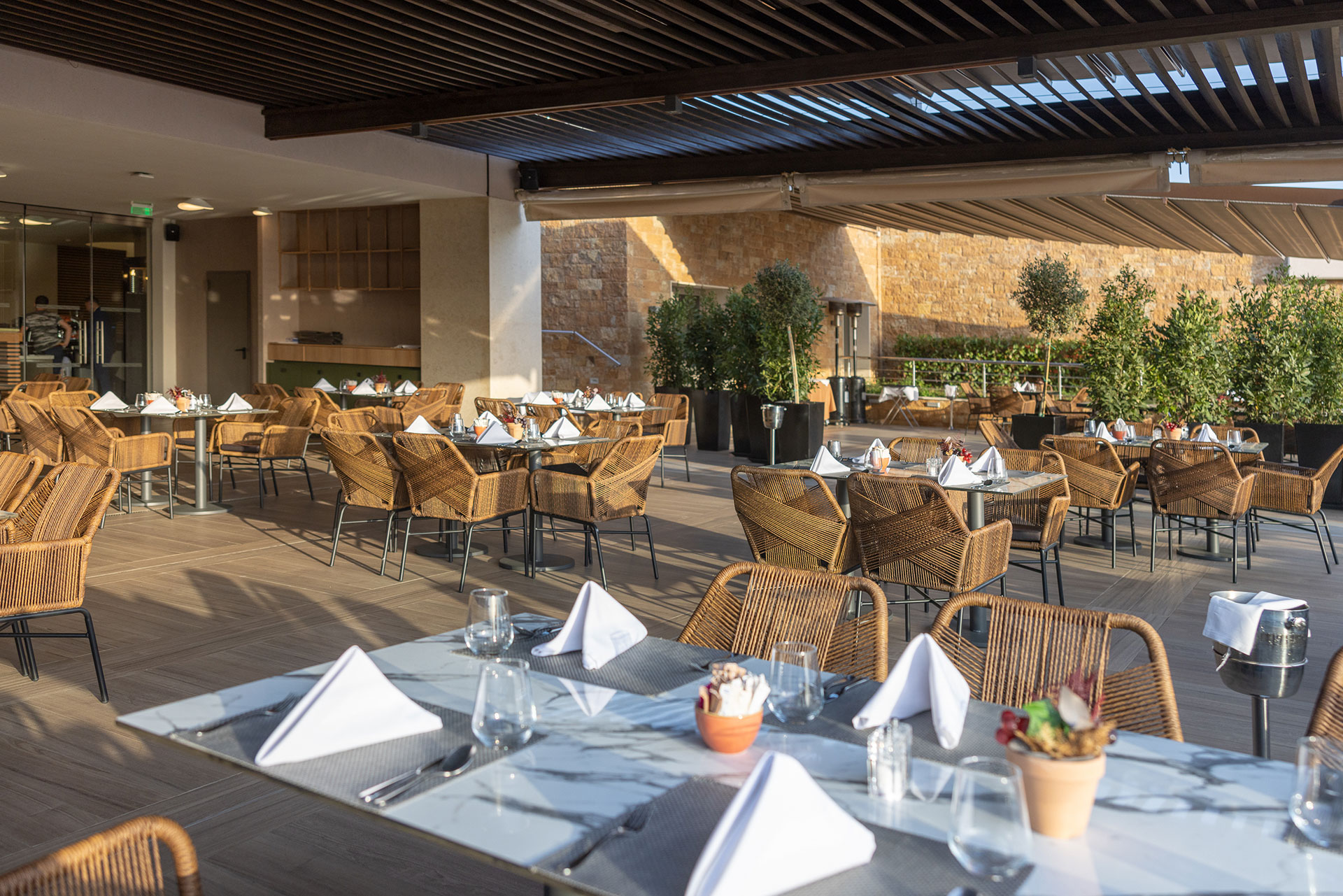 Elegant outdoor dining area of Elia restaurant with rattan chairs, marble tables and natural stone walls