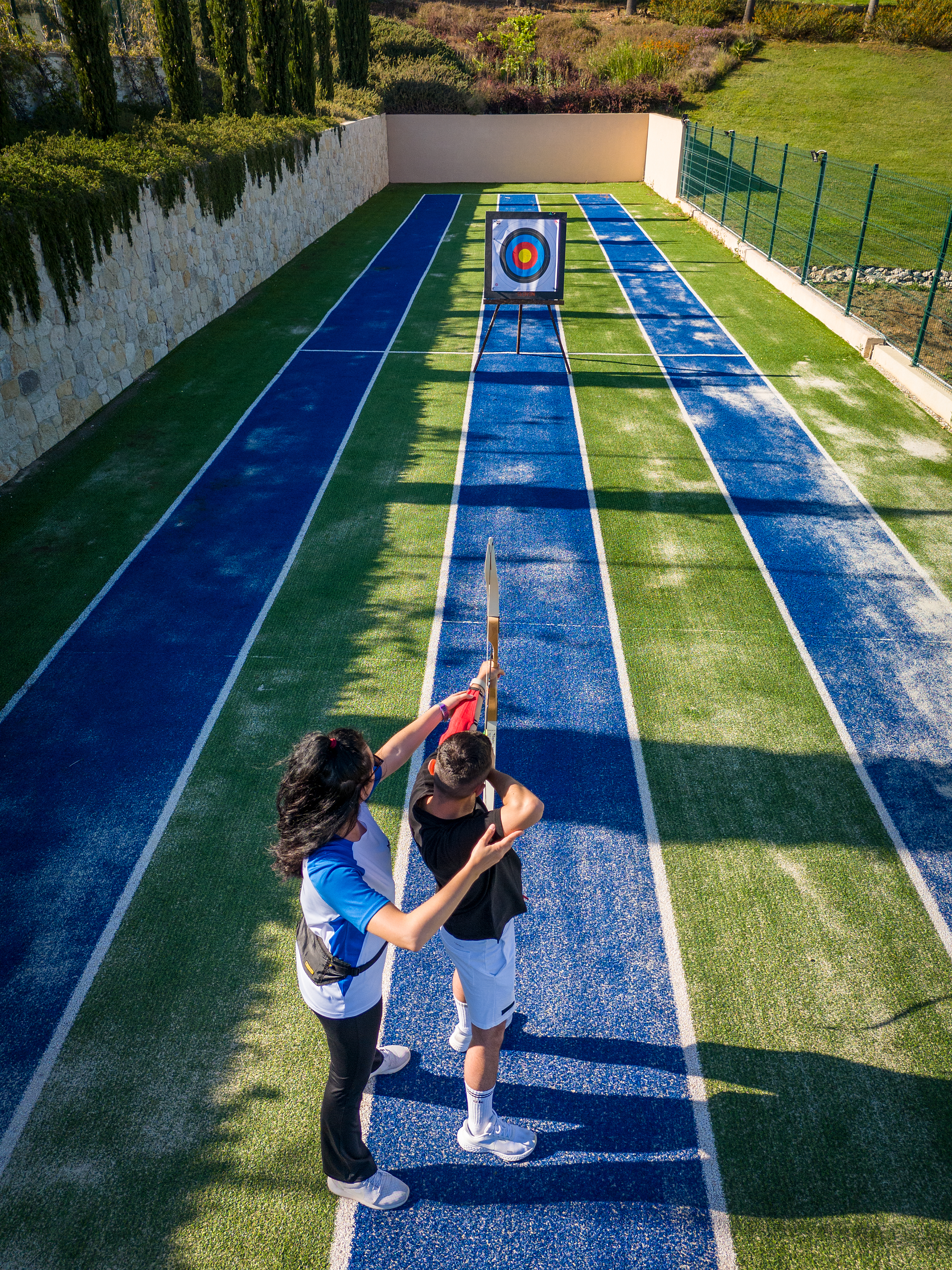 Archery instructor guiding guest's body posture to improve aim at the outdoor range