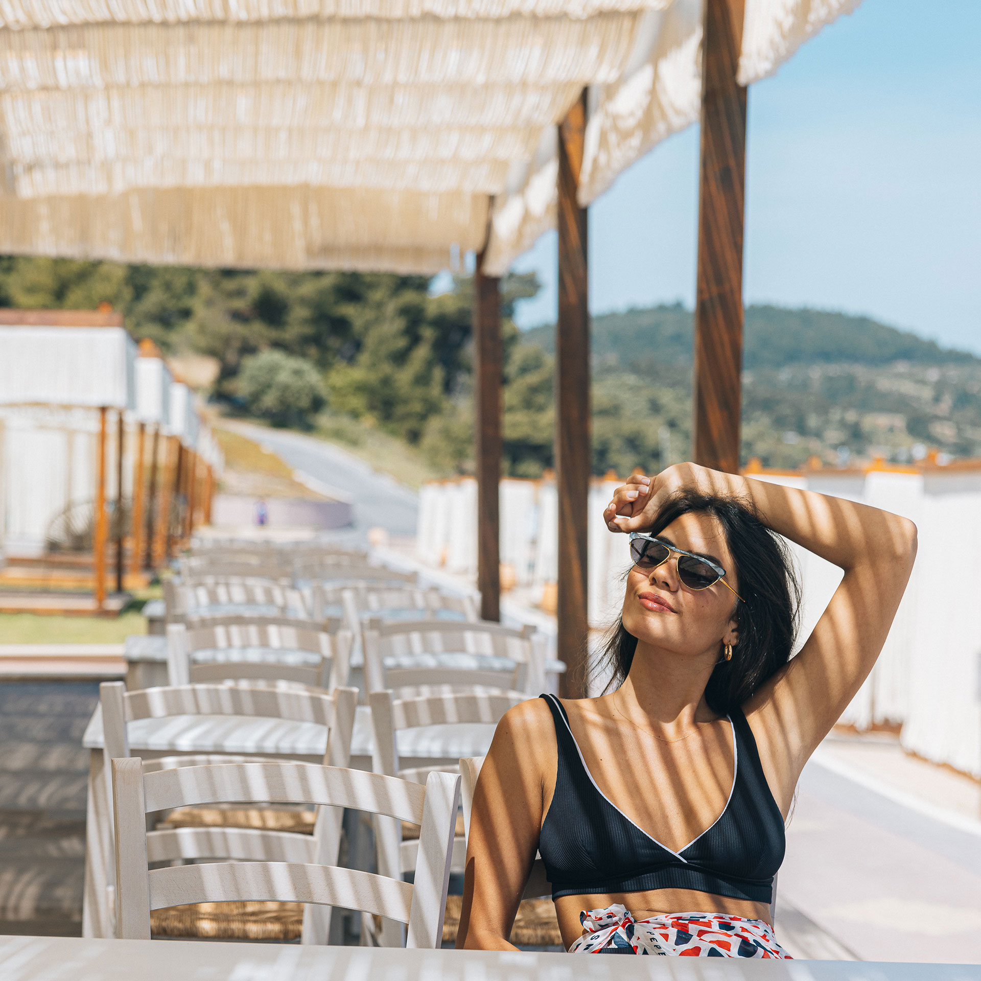 Woman relaxing at the outdoor seating of Mezedaki beach restaurant, enjoying the sea breeze