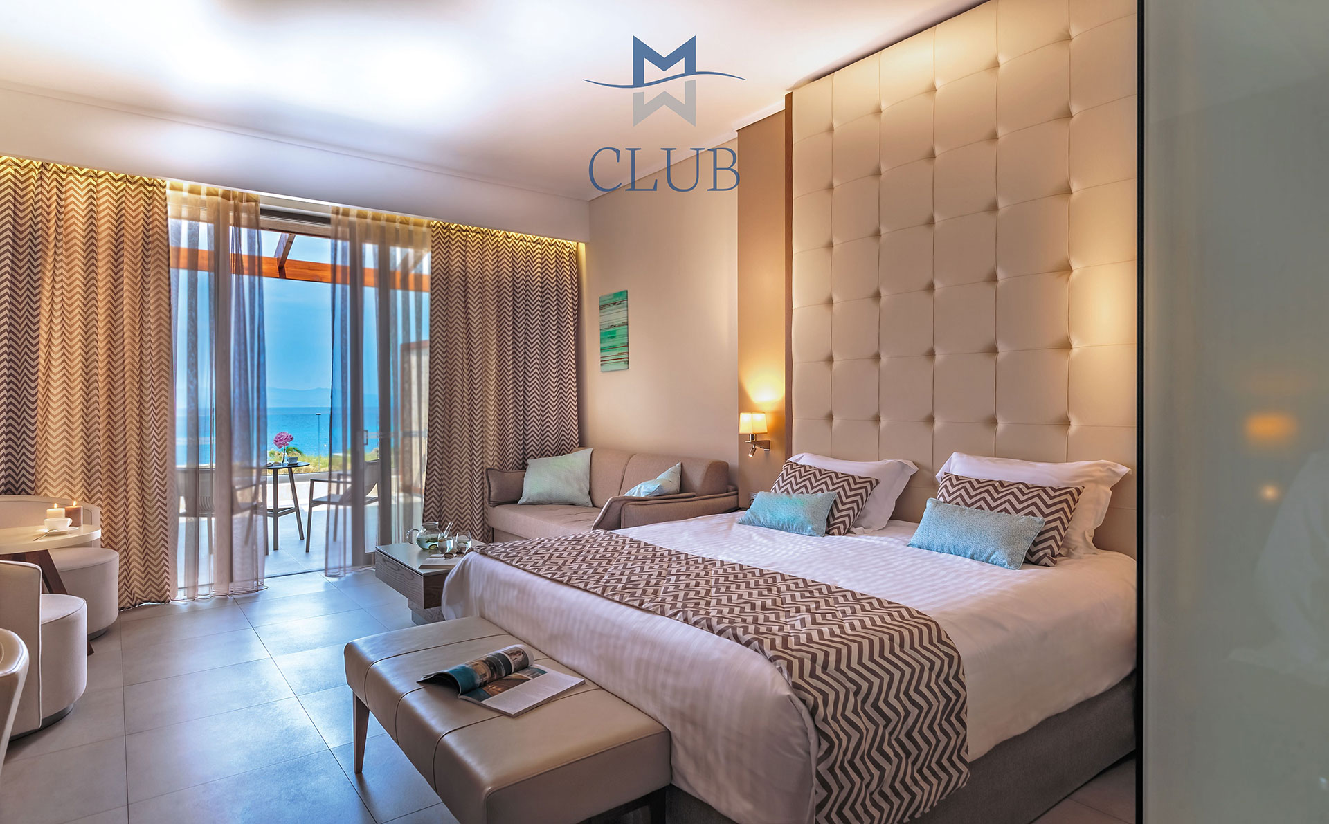 Modern sea view room with king size bed, cozy seating area with ambient lighting and glass doors overlooking the sea