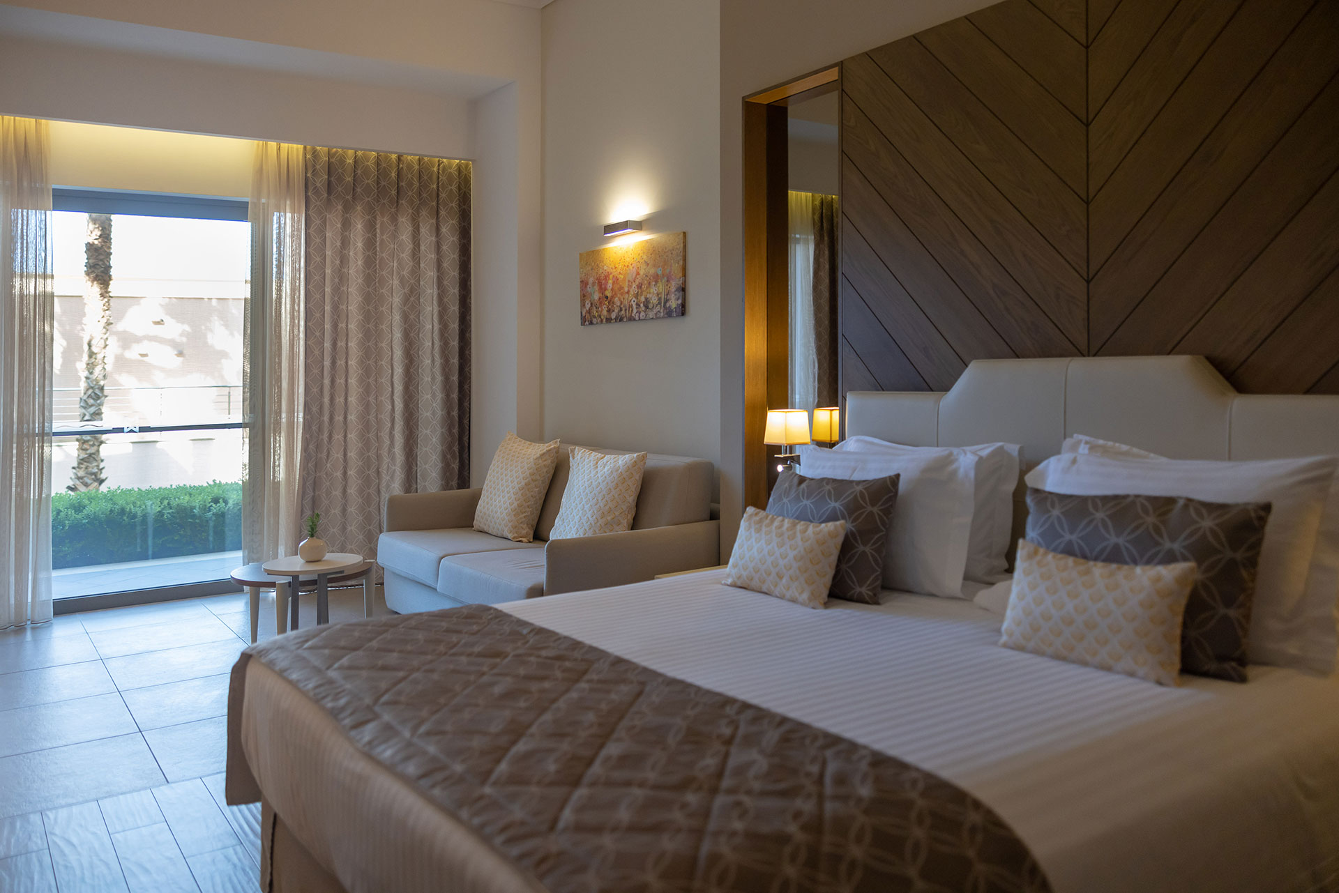 Deluxe room with elegant king bed, soft lighting and cozy sofa near the terrace