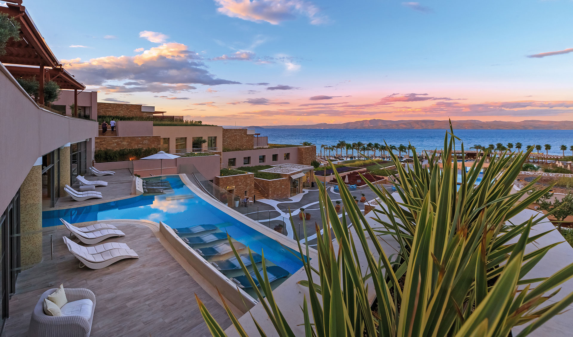 Infinity pool with lounge chairs overlooking the Aegean Sea at sunset