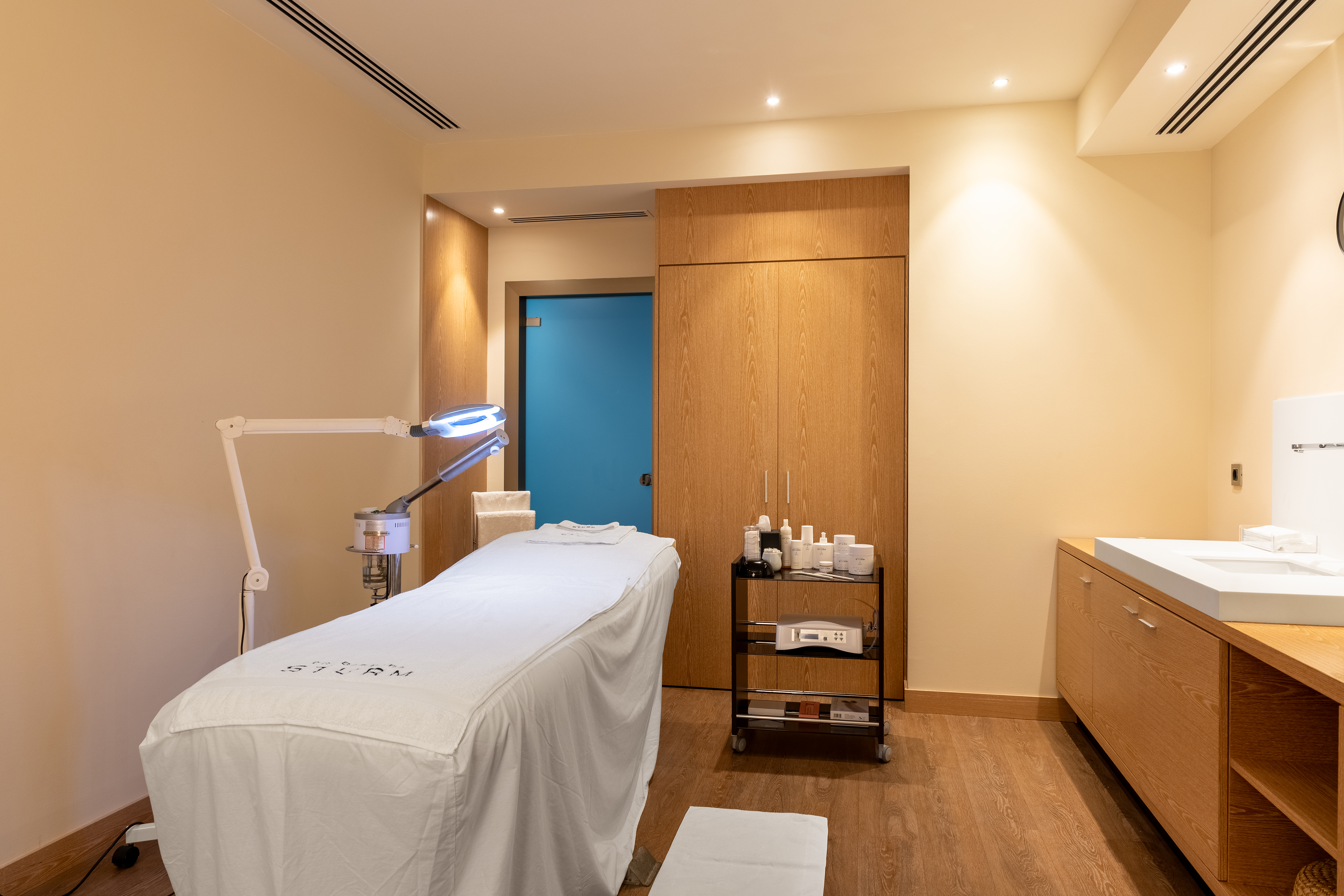 Spa treatment room with bed, magnifying lamp and trolley with skincare products