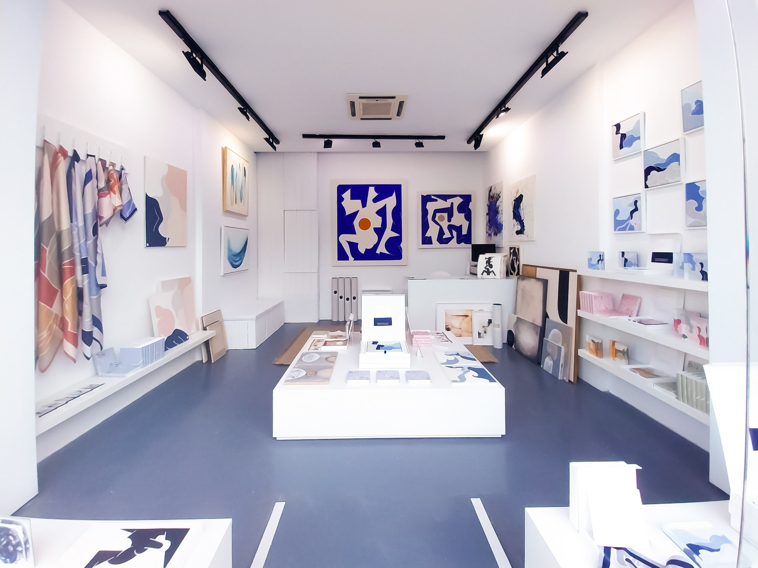 Interior of art gallery with abstract blue toned paintings and pastel scarves on display