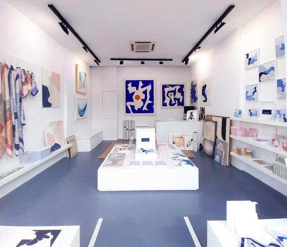 Interior of art gallery with abstract blue toned paintings and pastel scarves on display