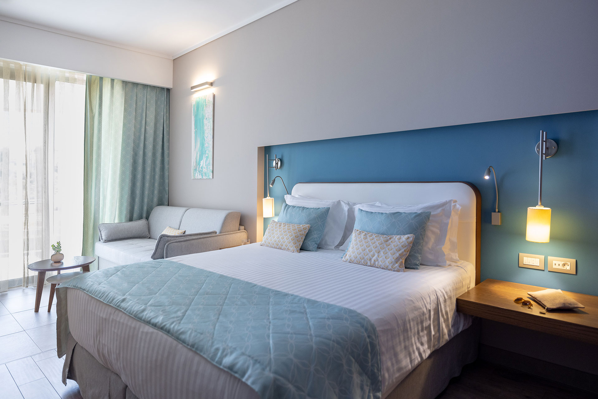 Elegant deluxe room with king bed, soft blue accents, and natural light through balcony doors