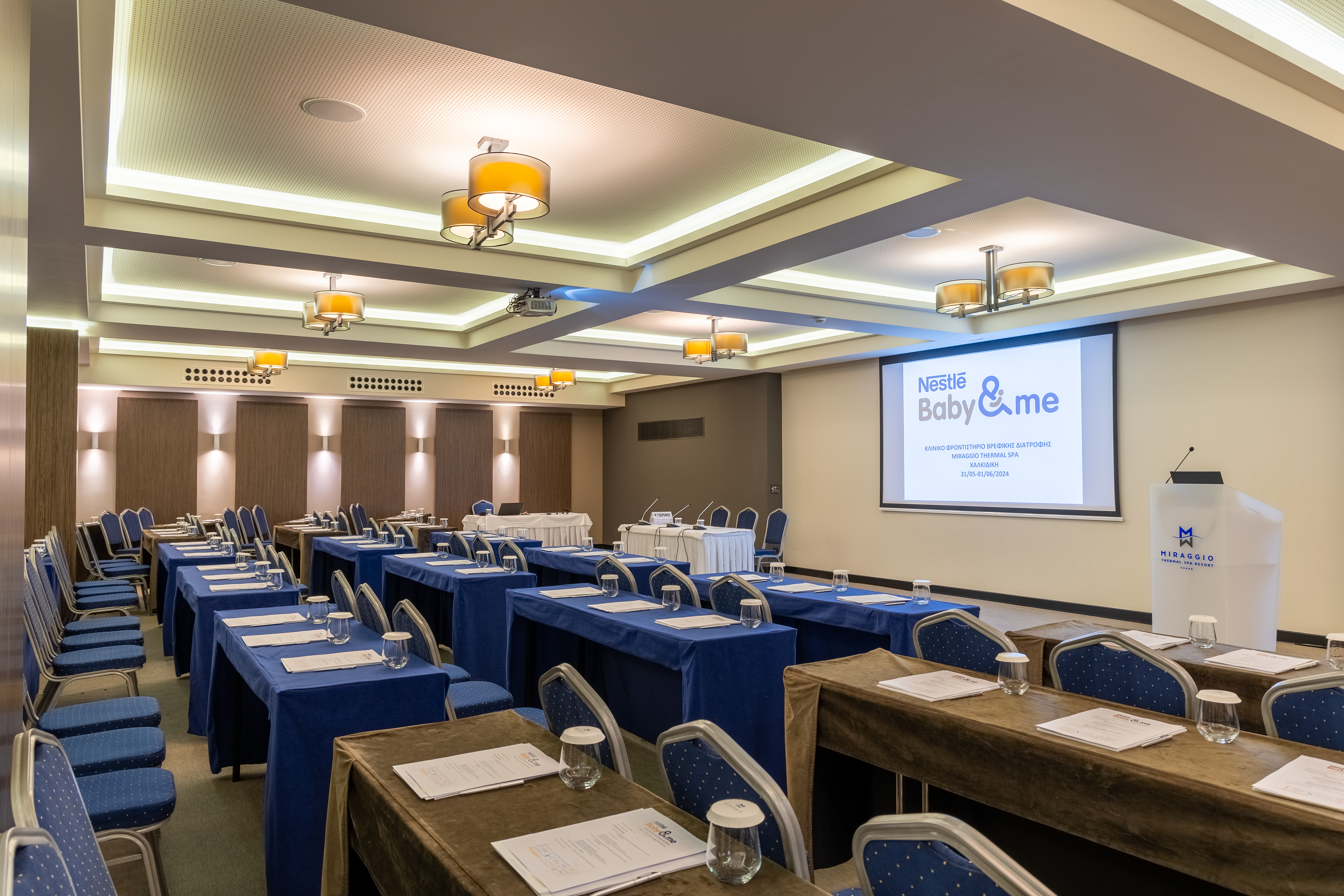 Conference setup with presentation screen, blue-covered tables, and neatly arranged chairs for a professional seminar