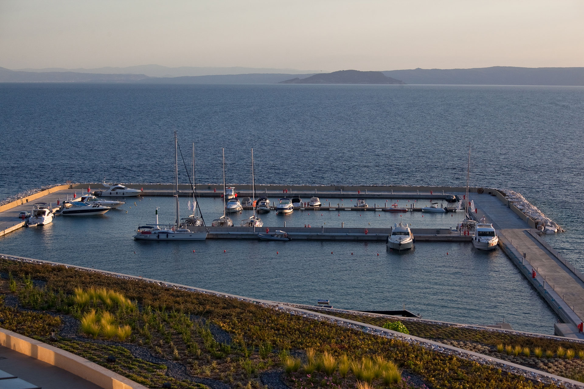 View of yachts moored at the marina with calm sea and mountain backdrop during golden hour