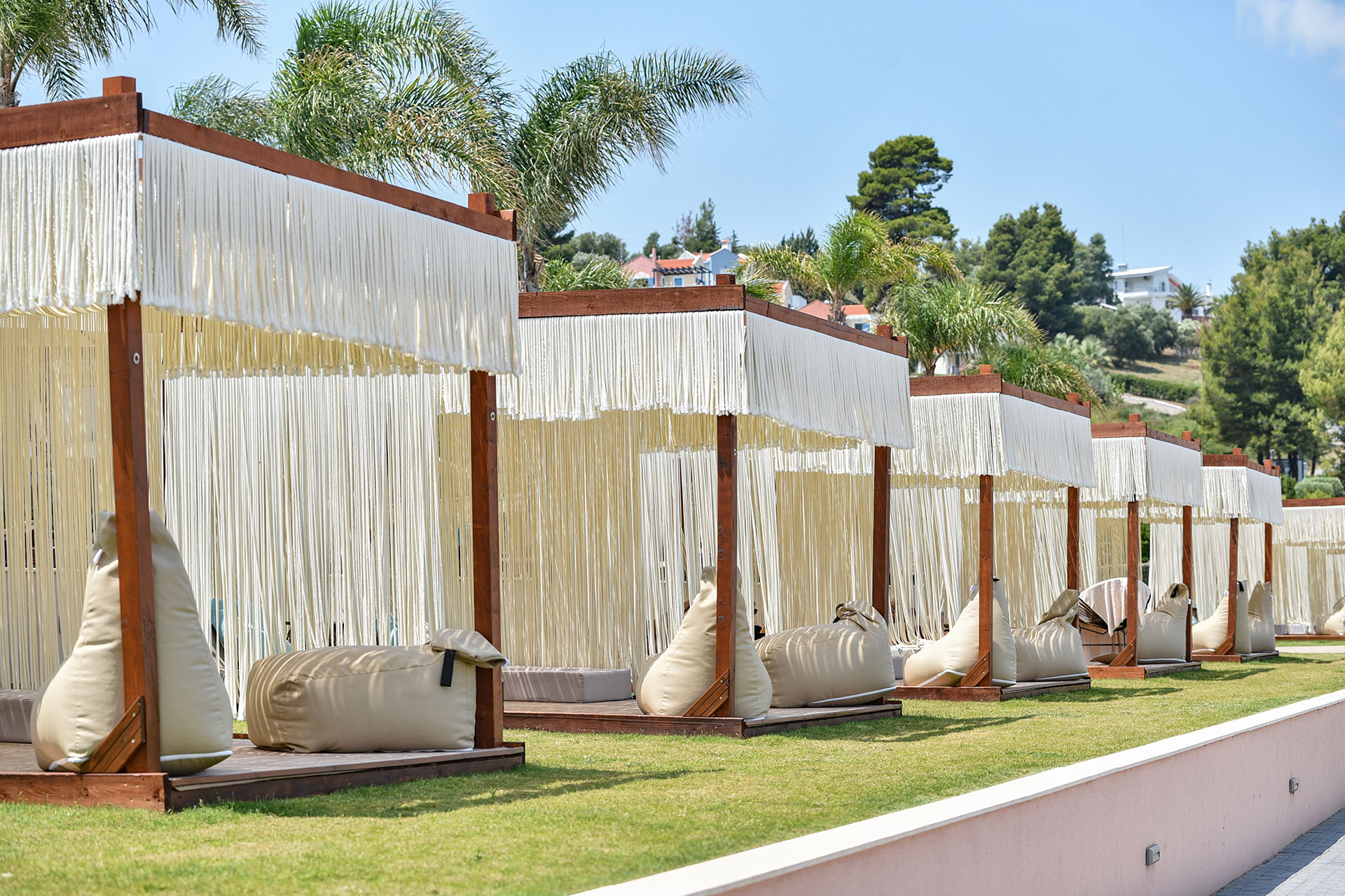 Row of elegant cabanas with white fringe canopies and lounge seating amid palm trees