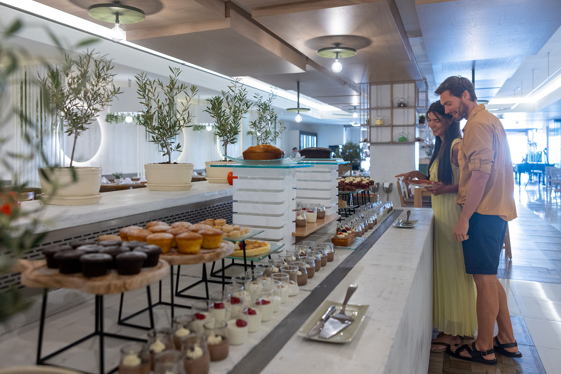 Couple choosing from a buffet of cakes and desserts decorated with olive plants