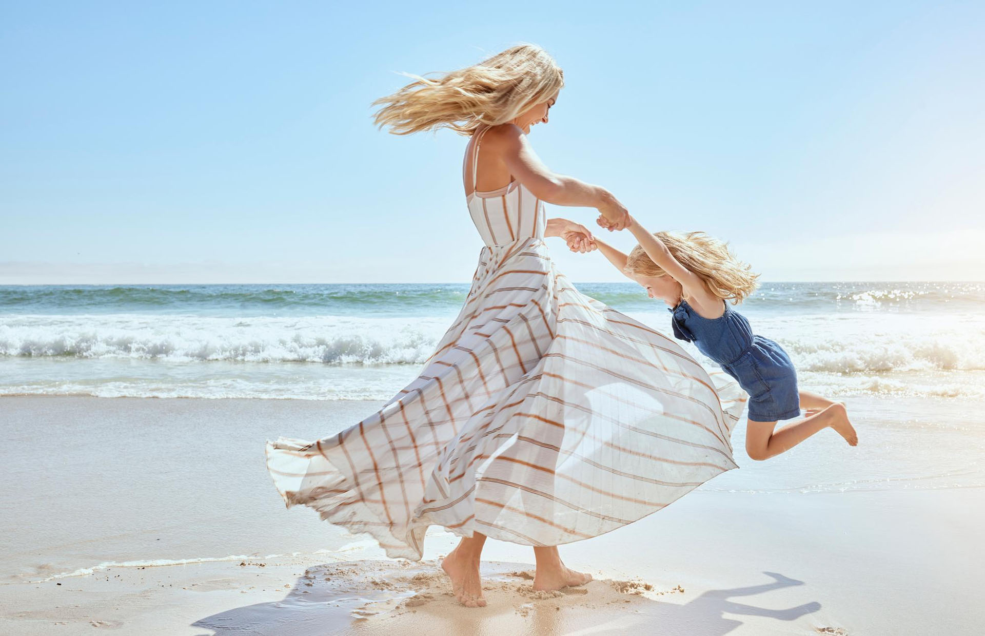 Mother and daughter playing joyfully on a sandy beach under bright sunlight
