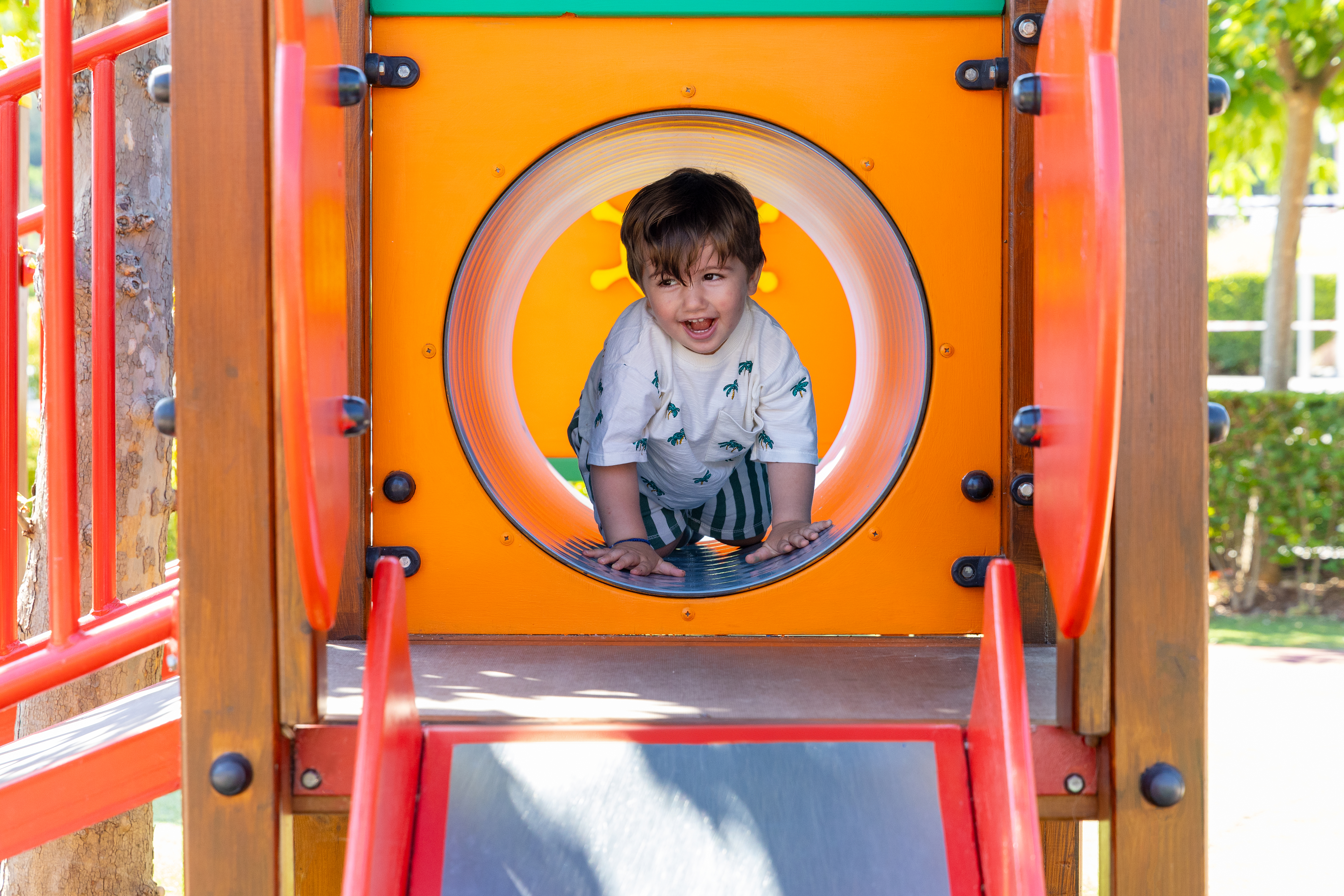 Toddler crawling through a colorful playground tunnel slide in Kids Planet playground