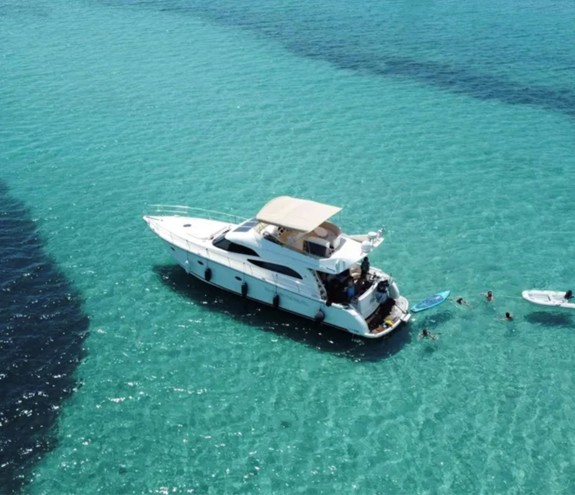 Luxury yacht anchored in shallow turquoise water with guests swimming and paddleboarding around it